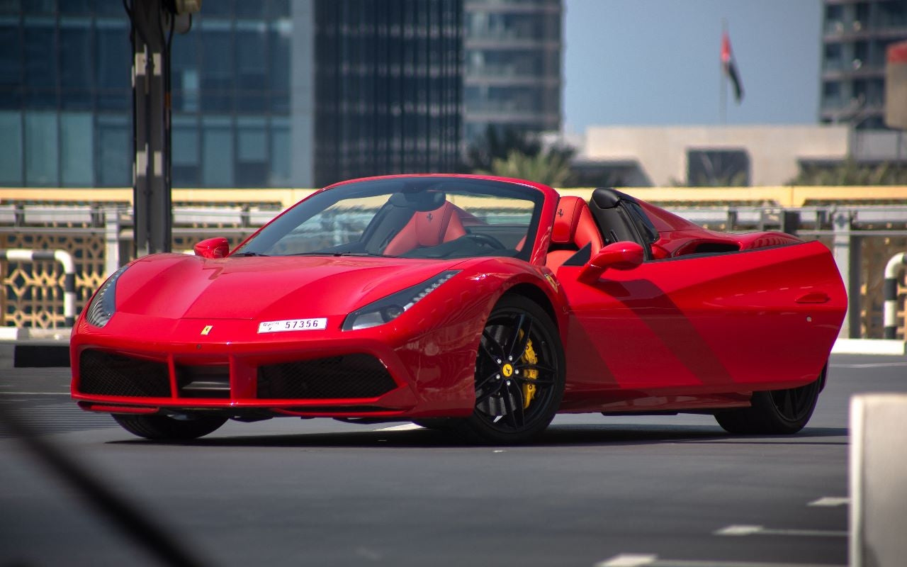 Red Ferrari 488 Spyder luxury sports car for rent in Dubai, showcasing its sleek profile and aerodynamic design.